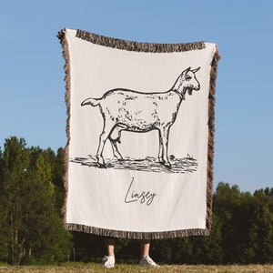 Pu&ograve; includere: Una coperta in tessuto bianco con un'illustrazione in bianco e nero di una capra e il nome "Lindsey" scritto in corsivo.