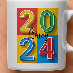 May include: White ceramic mug with a colorful design featuring the numbers 2024 in a retro style. The name "Lindsey" is written in black cursive script on the mug.