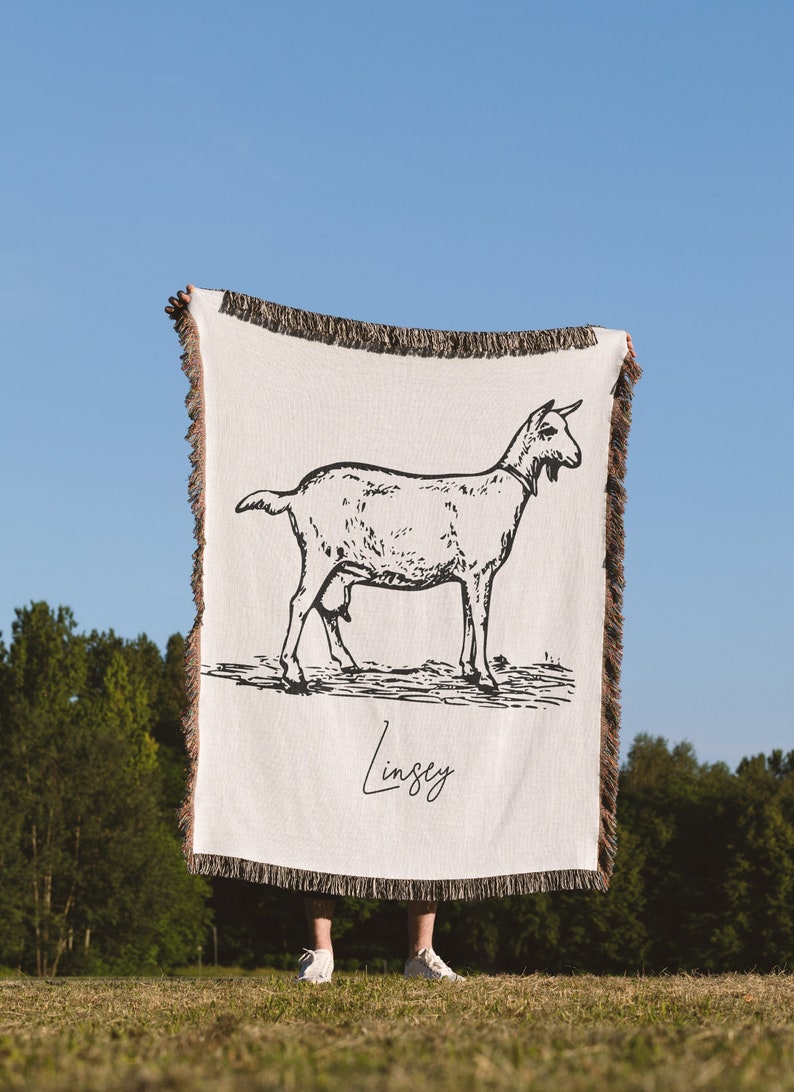 Pu&ograve; includere: Una coperta in tessuto bianco con un'illustrazione in bianco e nero di una capra e il nome "Lindsey" scritto in corsivo.