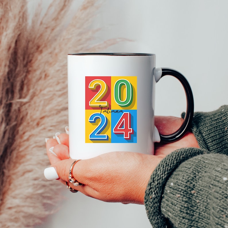 May include: White ceramic mug with a black handle. The mug has a colorful design with the numbers 20 and 24 in a block style font. The text "Tatiana" is written in cursive between the numbers.