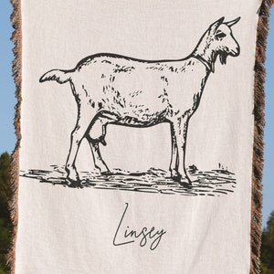Pu&ograve; includere: Una coperta in tessuto bianco con un disegno a linea nera di una capra e il nome "Lindsey" scritto in corsivo.