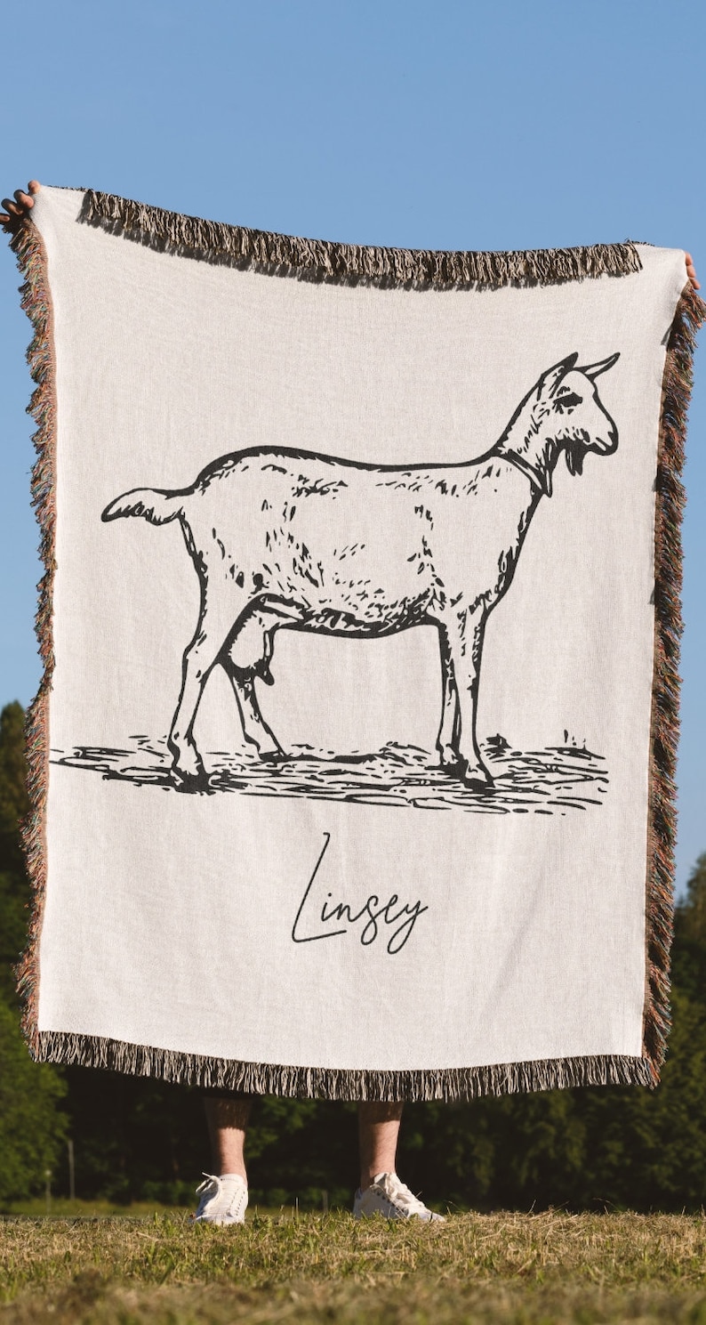 Pu&ograve; includere: Una coperta in tessuto bianco con un disegno a linea nera di una capra e il nome "Lindsey" scritto in corsivo.