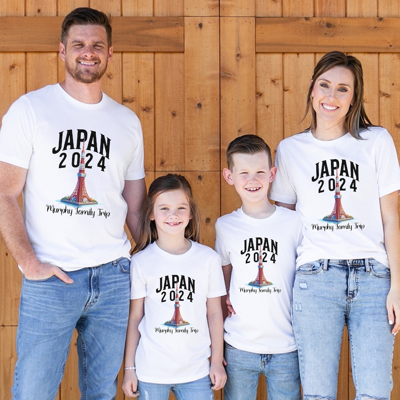 K&ouml;nnte beinhalten: Eine vierk&ouml;pfige Familie tr&auml;gt wei&szlig;e T-Shirts mit einem Grafikdruck eines roten und wei&szlig;en Leuchtturms und dem Text "JAPAN 2024" und "Murphy Family Trip".
