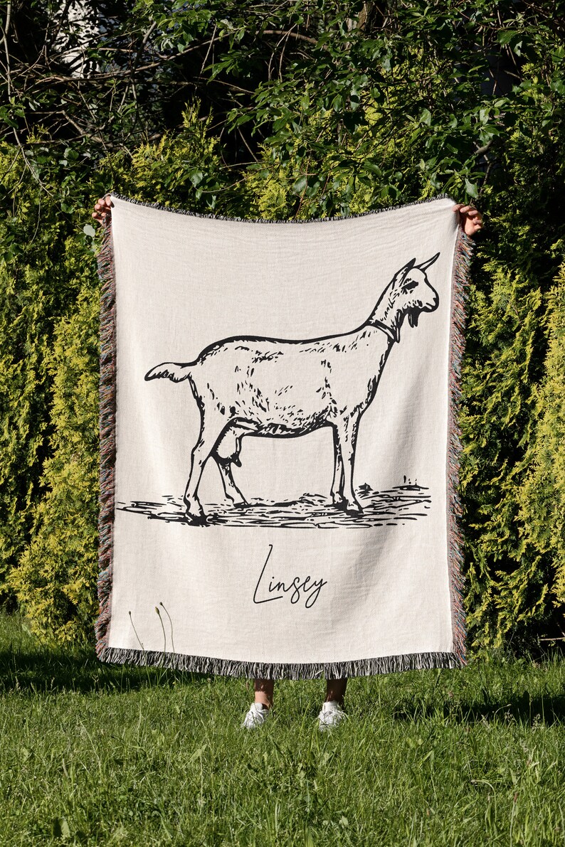 Pu&ograve; includere: Una coperta in tessuto di stile arazzo con un'illustrazione in bianco e nero di una capra e il nome "Lindsey" scritto in corsivo.