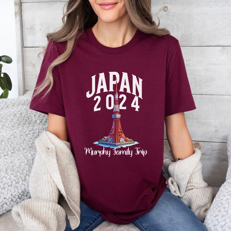 K&ouml;nnte beinhalten: Ein maroonfarbenes T-Shirt mit wei&szlig;em Text, der "JAPAN 2024" lautet, und einer Grafik des Tokyo Towers. Unter dem Turm steht der Text "Murphy Family Trip".