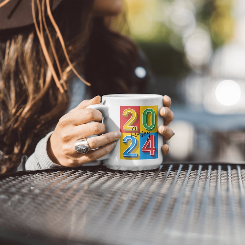May include: White ceramic mug with a colorful design featuring the numbers 2024 and the name "Lindsey" in a script font.