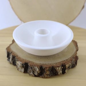 May include: A white ceramic incense holder with a central raised cylinder, resting on a rustic, circular wooden slice. The holder's design is simple and minimalist, perfect for home decor and aromatherapy.