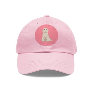 May include: A pink baseball cap with a round, pink patch featuring a white doodle of a dog sitting.