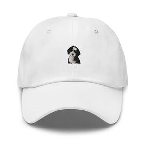 May include: A white baseball cap featuring a small, centered embroidered graphic of a black, white, and brown dog. The cap has a structured crown, a curved brim, and a button at the top, providing a clean and simple look for everyday headwear.