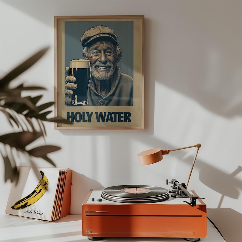 May include: A framed poster with the text "HOLY WATER" features a smiling elderly man holding a glass of dark beer. A vintage orange record player with a vinyl record is on a white surface.
