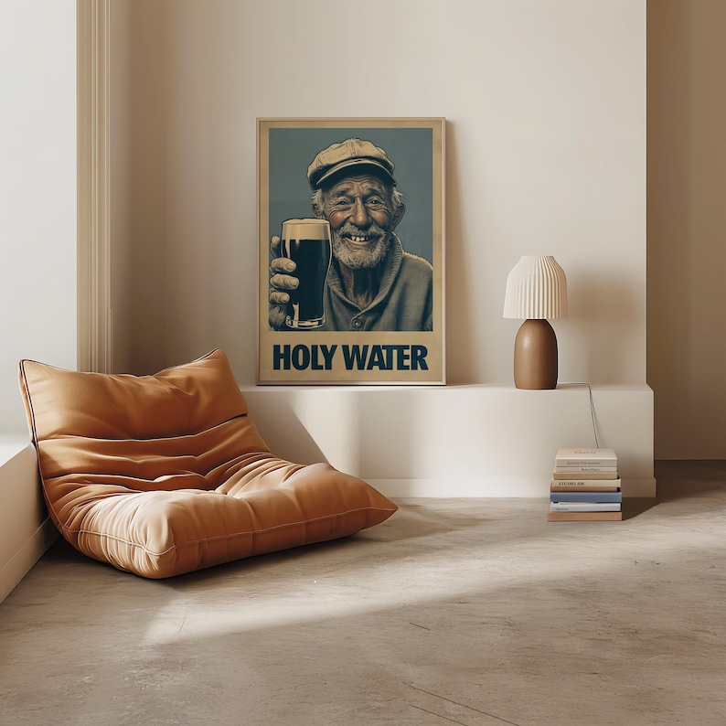 May include: A framed poster featuring an elderly man holding a pint of dark beer, with the text "HOLY WATER" below. The man is smiling and wearing a cap. The poster is displayed in a room with a brown beanbag chair and a small lamp.