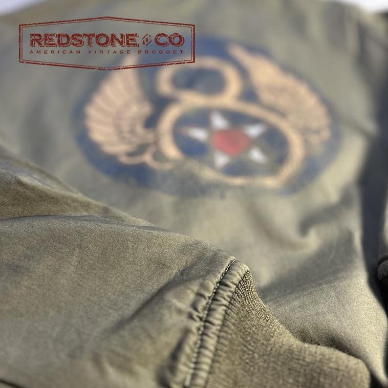 May include: An olive green bomber jacket with a vintage military patch featuring a star and wings. The jacket has a ribbed cuff. The text "REDSTONE & CO AMERICAN VINTAGE PRODUCT" is visible.