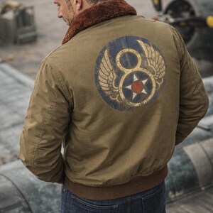 May include: Olive green bomber jacket with a brown faux fur collar and a circular patch on the back. The patch features a blue circle with a white star and the number 8, flanked by wings. The jacket has a ribbed hem and cuffs.