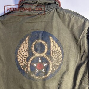 May include: An olive green jacket with a circular emblem featuring wings, a number eight, and a star. The jacket has a fur-lined hood. The text "REDSTONE & CO" is visible. Vintage style.