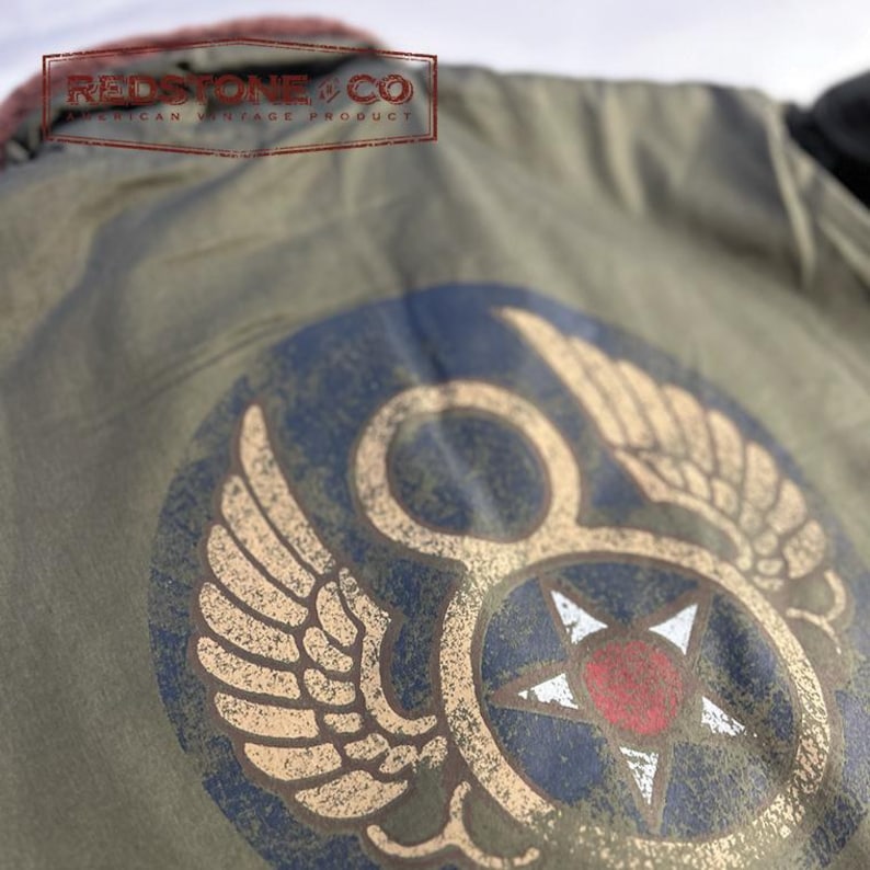 May include: An olive green jacket with a distressed design. The jacket has a large emblem with wings, a star, and the number 8 in a circle. The text "REDSTONE & CO AMERICAN VINTAGE PRODUCT" is visible.