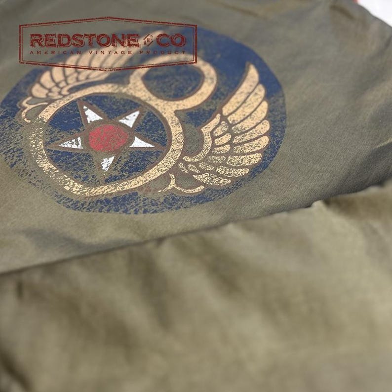 May include: Olive green fabric with a distressed vintage design. A circular emblem features a star within a blue circle, flanked by wings. The emblem is printed in gold and red. The text "REDSTONE & CO AMERICAN VINTAGE PRODUCT" is printed at the top.