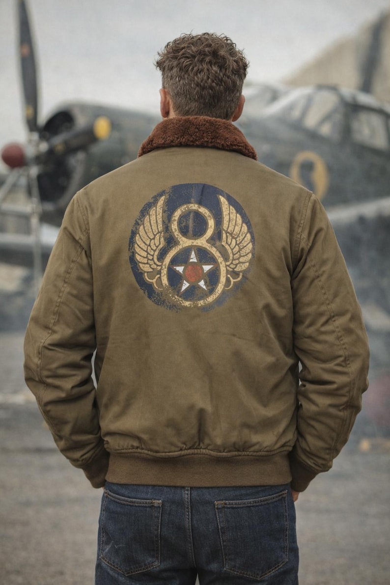 May include: An olive green bomber jacket with a brown fur collar. The back of the jacket displays a circular emblem with wings, the number 8, and a star. The person is wearing blue jeans. An aeroplane is in the background.