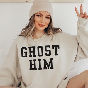 May include: A light beige sweatshirt with the text "GHOST HIM" printed in black.