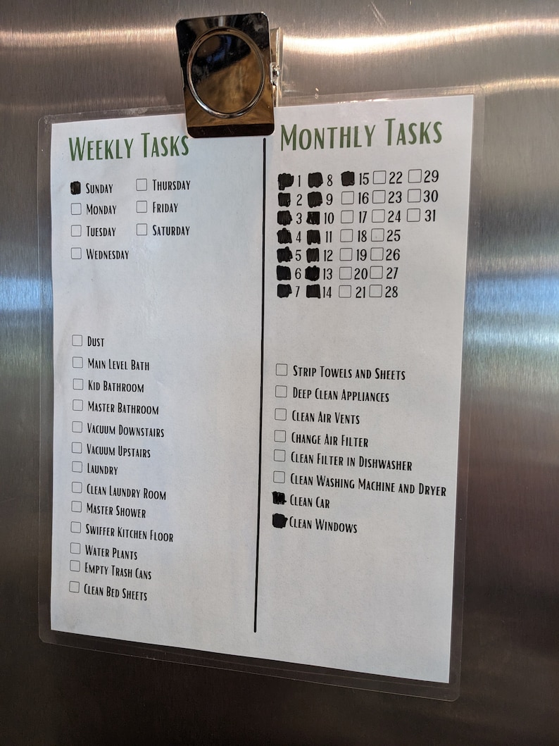 Puede incluir: Una lista de tareas semanales y mensuales en un refrigerador de acero inoxidable. La lista se titula "Tareas semanales" y "Tareas mensuales". Las tareas semanales incluyen "Polvo", "Ba&ntilde;o del nivel principal", "Ba&ntilde;o de los ni&ntilde;os", "Ba&ntilde;o principal", "Aspirar las escaleras de abajo", "Aspirar las escaleras de arriba", "Lavander&iacute;a", "Limpiar la sala de lavander&iacute;a", "Ducha principal", "Fregar el piso de la cocina", "Regar las plantas", "Vaciar los botes de basura", y "Cambiar las s&aacute;banas". Las tareas mensuales incluyen "Cambiar las toallas y las s&aacute;banas", "Limpiar a fondo los electrodom&eacute;sticos", "Limpiar las rejillas de ventilaci&oacute;n", "Cambiar el filtro de aire", "Limpiar el filtro del lavavajillas", "Limpiar la lavadora y la secadora", "Lavar el coche", y "Limpiar las ventanas".