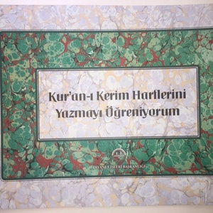 Puede incluir: Una cubierta de mármol verde y rojo con un borde blanco y el texto "Kur'an-i Kerim Harflerini Yazmayi Ögreniyorum" en negro. El texto "Diyanet Isleri Baskanligi" está en negro en la parte inferior de la cubierta.