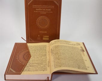 May include: Three brown hardcover books are displayed, one open to show handwritten text. The covers feature gold lettering and a circular design. The book's title is "SAHİH-İ BUHÂRİ". A bookmark is visible in the open book.