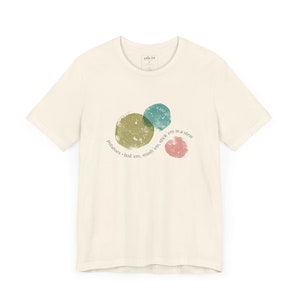 Op de afbeelding: Een crèmekleurig t-shirt met een afbeelding van drie gekleurde cirkels en de tekst "potatoes - boil 'em, mash 'em, stick 'em in a stew".