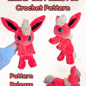 May include: A crochet pattern release showcasing a red and cream-coloured Ember the Flame Fox plushie. The plushie has large blue eyes, black-tipped ears, and a fluffy cream-coloured mane. The text "Ember the Flame Fox Crochet Pattern" and "Pattern Release" are displayed.
