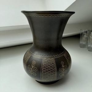 May include: A black ceramic vase with a geometric design and floral accents. The vase has a wide mouth and a narrow base.