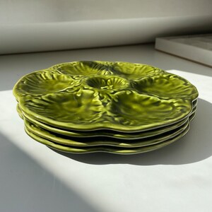 Può includere: Un set di tre piatti per ostriche in ceramica verde. I piatti sono impilati uno sopra l'altro e hanno un bordo ondulato.
