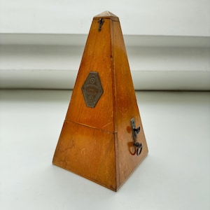 Può includere: Un metronomo in legno con una placca in ottone che recita "Maelzel's Patent Metronome". Il metronomo ha la forma di una piramide e ha una chiave per caricarlo.