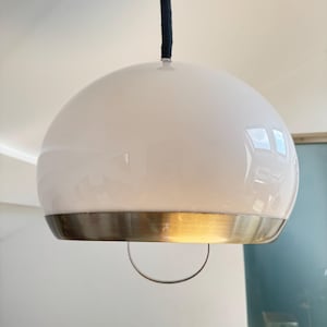 May include: A white, dome-shaped pendant light with a brushed metal band at the base. The light hangs from a black cord. The design is modern and minimalist, suitable for various interior styles.