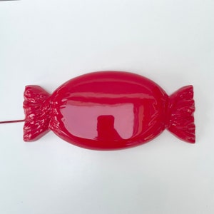 May include: A red candy-shaped wall decor with a glossy finish. The decor is shaped like a wrapped candy with a ruffled edge.