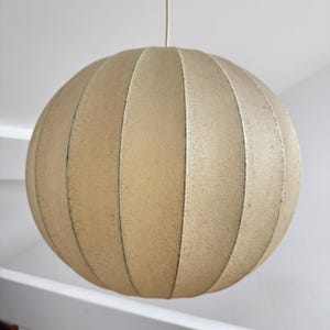 May include: A beige, spherical pendant light fixture. The light has a ribbed design, with vertical panels creating a segmented globe shape. The light hangs from a thin, off-white cord.