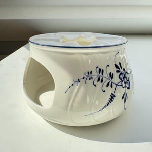 Może przedstawiać: Biały ceramiczny podgrzewacz do herbaty z niebieskim wzorem kwiatowym. Podgrzewacz ma otwór w środku, na którym można umieścić czajnik.
