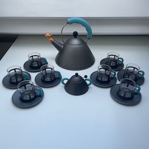 Puede incluir: Un juego de té negro y azul con una tetera, un azucarero y seis tazas. La tetera tiene un asa y un pico azul, y las tazas tienen asas y bordes azules.