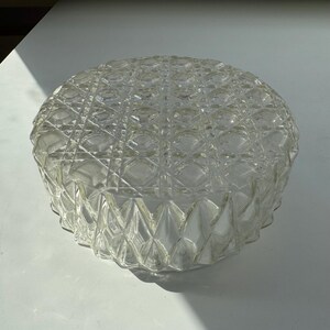 May include: A clear glass ceiling light fixture with a geometric pattern. The light fixture is round and has a textured surface.