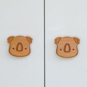 Peut inclure: Deux poignées de tiroir en bois en forme de koala avec une finition brun clair. Les koalas ont un design simple avec un nez, des yeux et des oreilles.