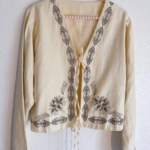 May include: A white ceramic mug with a black handle and the text "But First, Coffee" in a bold, black font. The mug is set against a blurred background, suggesting a cozy setting.