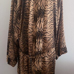 May include: A brown and black tiger-striped robe with long sleeves and a matching belt. The robe is displayed on a mannequin. The fabric has a silky appearance. The robe is knee-length.