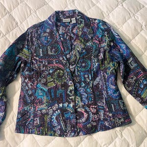 May include: A patterned blazer in shades of blue, purple, green, and pink. The jacket has a button closure and long sleeves. The fabric has a quilted texture and a paisley-like design.