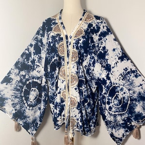 May include: A blue and white tie-dye kimono with gold and brown embroidery and tassels. The kimono has a V-neck and long sleeves.