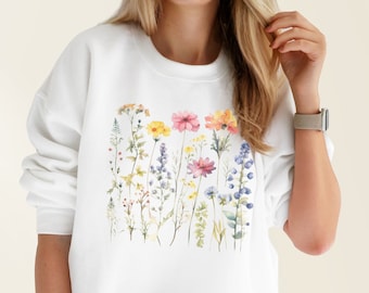 Könnte beinhalten: Weißer Pullover mit einem Aquarell-Blumenmuster mit rosa, gelben und blauen Blumen.