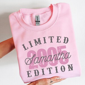 K&ouml;nnte beinhalten: Ein hellrosa Sweatshirt mit dem Text "LIMITED 2005 Samantha EDITION" in Grau und Rosa. Das Sweatshirt hat einen Rundhalsausschnitt und ist gefaltet. Das Bild zeigt ein Kleidungsst&uuml;ck.