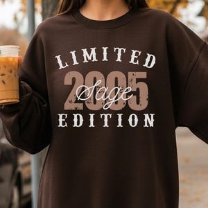 K&ouml;nnte beinhalten: Dunkelbraunes Sweatshirt mit dem Text "LIMITED 2005 Sage EDITION" in Wei&szlig; und Braun. Das Sweatshirt hat einen Rundhalsausschnitt. Das Bild zeigt auch ein Getr&auml;nk in einem transparenten Plastikbecher mit einem gr&uuml;nen Strohhalm.