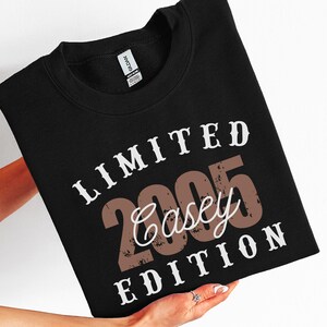 K&ouml;nnte beinhalten: Schwarzes Sweatshirt mit dem Text "LIMITED 2005 Casey EDITION" in Wei&szlig; und Braun. Das Sweatshirt hat einen Rundhalsausschnitt. Das Wort "SWEATER - BLACK" ist auf einem vertikalen Etikett auf der rechten Seite des Bildes aufgedruckt.