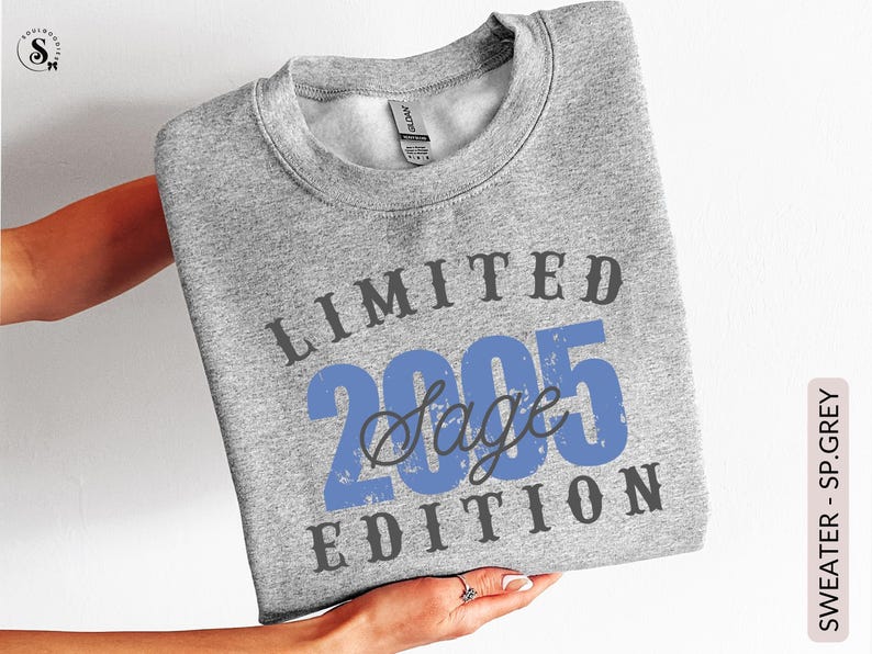 K&ouml;nnte beinhalten: Ein hellgraues Sweatshirt mit dem Text "LIMITED 2005 Sage EDITION" in Blau und Dunkelgrau. Das Sweatshirt wird von einer Person gehalten. Das Produkt ist mit "SWEATER - SP.GREY" gekennzeichnet.