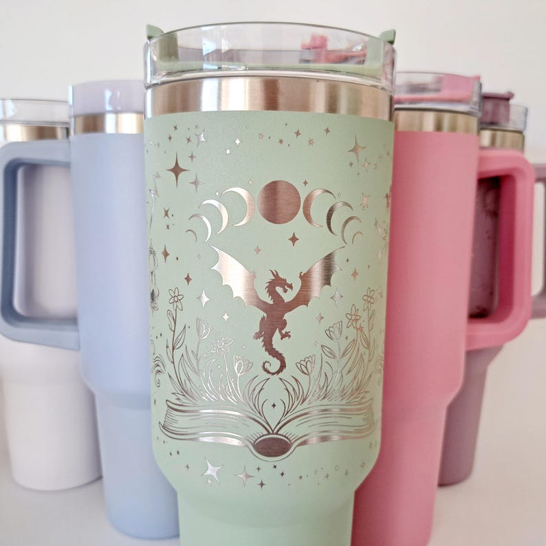 May include: A green stainless steel tumbler with a silver dragon and moon design. The tumbler has a lid and a handle.
