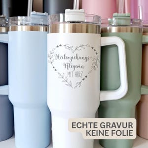 Könnte beinhalten: Eine Sammlung isolierter Becher in verschiedenen Farben, darunter Weiß, Hellblau und Grün. Der weiße Becher hat ein herzförmiges Design mit Text. Jeder Becher hat einen Griff, einen transparenten Deckel und einen Strohhalm. Der Text auf dem weißen Becher lautet "Heilerziehungs-Pflegerin MIT HERZ".