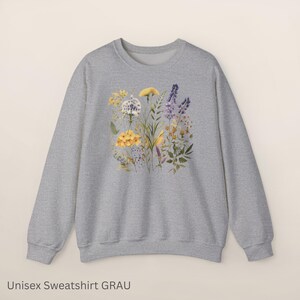 以下が含まれることがあります： 黄色、紫、白の水彩画の花柄が特徴の、明るい灰色のユニセックススウェットシャツ。スウェットシャツはクルーネックと長袖です。「Unisex Sweatshirt GRAU」というテキストが下にあります。