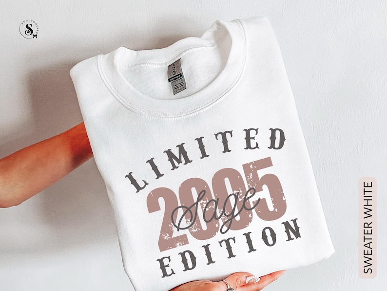 K&ouml;nnte beinhalten: Wei&szlig;es Sweatshirt mit dem Text "LIMITED 2005 Sage EDITION" in braunen und grauen Buchstaben. Das Sweatshirt wird von einer Person gehalten. Die Worte "SWEATER WHITE" sind vertikal auf der rechten Seite aufgedruckt.